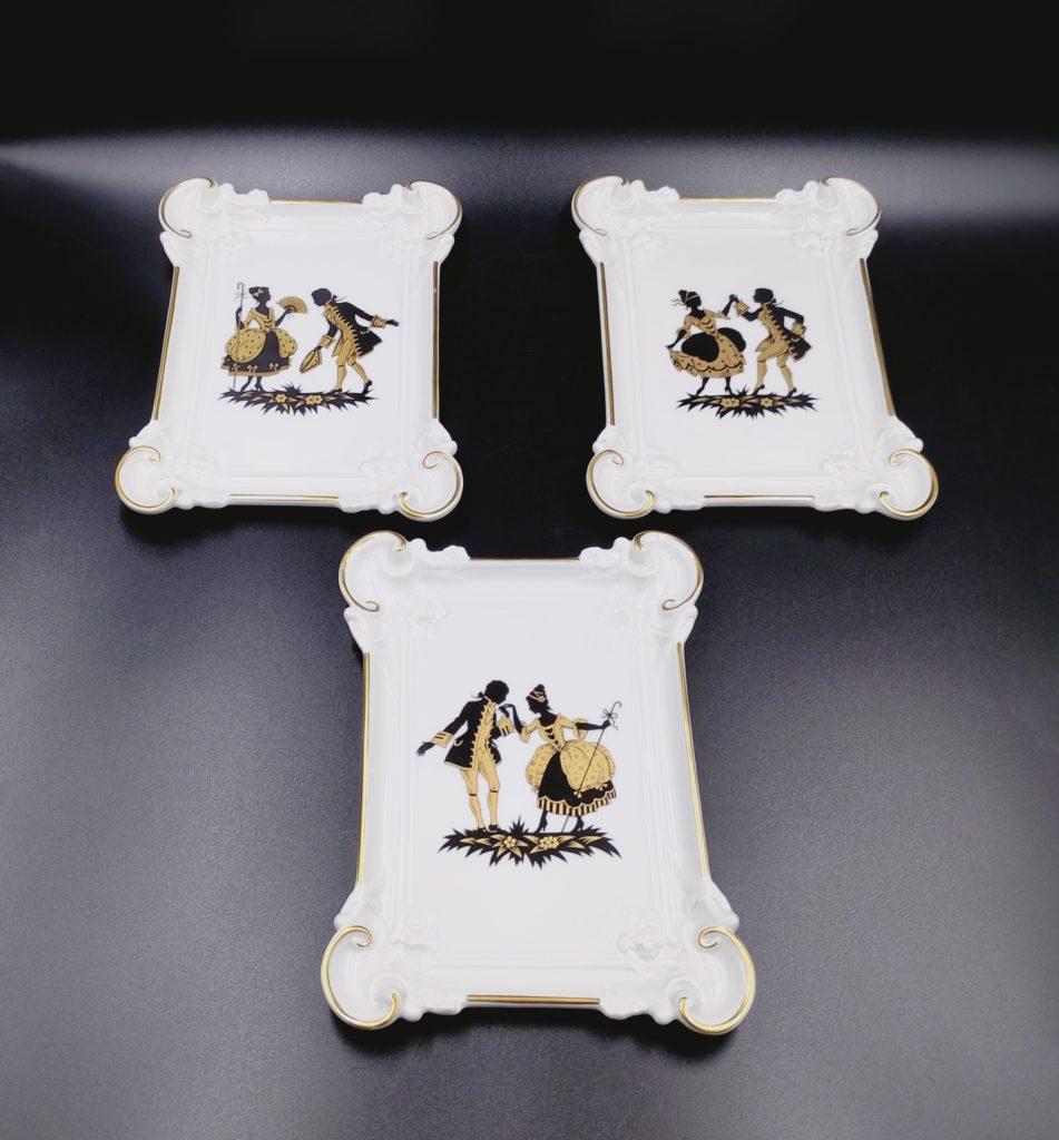 trzy deseczki obrazki Furstenberg wykonane z białej porcelany z z czarnymi i złotymi postaciami bogatym reliefem na rancie oraz  neorokokowym zdobienie,