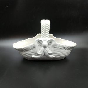 Biały ceramiczny koszyk na czarnym tle, koszyk posiada tłoczone zdobienia imitujące splot kosza oraz tłoczoną kokardę